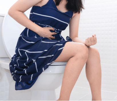 woman holding stomach on toilet pains in need of gastroenterologist